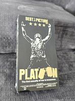 Front cover of sealed Platoon VHS tape showing soldier raising arms and movie title with Best Picture stars.