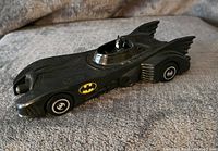 Side angle view of the Batmobile toy car showing Bat logos on the door and wheels, with visible rear fins and cockpit Batman figure.