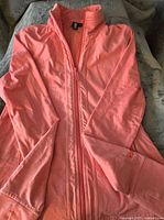 Coral-colored women's active jacket with full zipper folded on a blanket.
