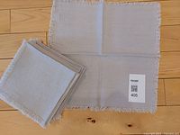 Set of folded and one spread light gray linen napkins, showing their size and texture.
