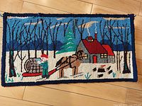 Full view of rectangular hooked rug showing winter scene with horse, man pulling sled, log cabin, trees, snow under light wooden floor.