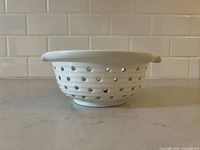 Side profile of the white ceramic strainer showing holes and rounded lip