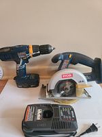 Ryobi cordless drill, circular saw, and battery charger arranged side by side.