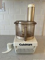 Cuisinart Mini-Prep food processor main unit with translucent brown container, feed tube and white chopping blade placed next to it on counter