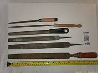 Six metal files arranged side by side showing variety of file shapes and handle styles, wood and plastic.