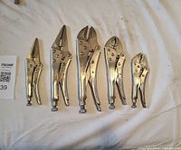 Five Mastercraft metallic locking pliers laid out on a white cloth showing various styles including curved jaw and long nose types
