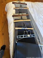 Photo showing six pairs of men's suit pants hung on hangers laid out in a row on a bed, showcasing different shades of grey and black.