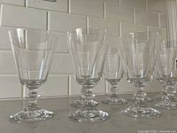 Front and side view of 8 clear parfait glasses arranged in a row showing flared bowl and pedestal base.
