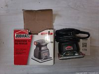 Box and Jobmate sheet sander side by side on white surface showing front and side of sander with label visible on box.