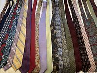 Photo showing 23 silk ties with different color and pattern variations, mostly laid out side by side on a bedsheet.