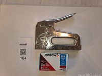 Metal Arrow T-50P heavy duty staple gun with box of staples in front of a neutral background.