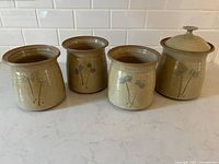 Four vintage pottery pots arranged in a row showing shape, size, and blue flower decoration