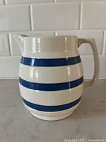 Side view of the vintage Staffordshire stoneware pitcher with blue horizontal stripes on a cream background, showing the spout and handle.