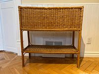 Front view of wicker plant stand showing rectangular woven wicker basket and lower shelf with legs.