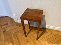 Front view of the small wooden end table showing slender straight legs and smooth top surface with natural wood grain.