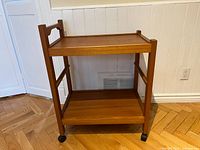 Front view of the wooden rolling stand showing two shelves, four vertical posts, and caster wheels.