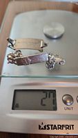 Two engraved sterling silver bracelets shown on a scale indicating a total weight of 27 grams.