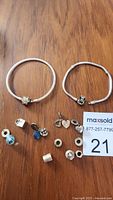 Two sterling silver Pandora ALE 925 bracelets with assortment of charms and spacers on wooden surface.