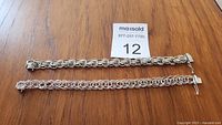 Two sterling silver charm bracelets displayed flat on wooden surface showing chain details and clasp.