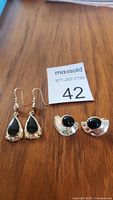 Two sets of sterling silver earrings on wood surface: teardrop black stone earrings and round black stone half-moon earrings.