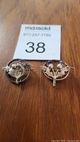 Two Scottish thistle brooches laid flat on a wooden surface with a maxsold auction number card.