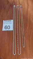 Photo showing three sterling silver chains laid flat on wooden surface with tags