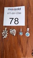 Four sterling silver pendants laid out on wooden surface: crown and heart design, etched heart locket, and two blue gemstone round pendants.