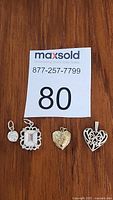Four sterling silver pendants displayed on wooden surface with MaxSold lot card