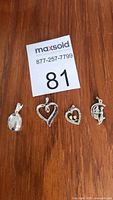 Four sterling silver pendants arranged in a row on a wooden surface, displayed next to a MaxSold card numbered 81.