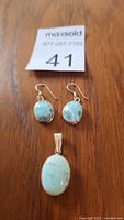 Photo showing pair of larimar stone drop earrings and matching pendant on wood surface with maxsold lot number 41.