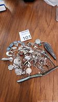 Full view of assorted silver scrap items laid on wooden surface including bracelets, rings, pendants, chains, and a barrette.