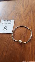 Photo showing the full silver bracelet lying flat on wood surface with maxsold lot number card.