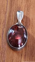 Front view of the oval amber stone set in sterling silver pendant on wooden background.