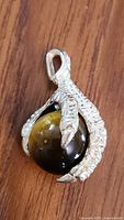 Close-up front view of sterling silver claw pendant holding Tiger's Eye stone on wooden surface.
