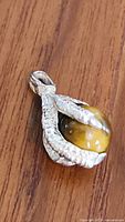 Front angled view of the sterling silver claw pendant holding a round Tiger's Eye stone on wooden surface.