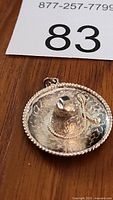 Close-up photo of silver sombrero pendant showing floral engravings and twisted rope detail around brim