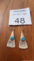 Close-up photo of two vintage sterling silver and turquoise drop earrings on wooden surface with lot number 48 tag.