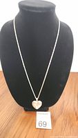 Full view of the necklace with heart-shaped locket on black display stand.