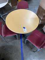 View showing round table top with light wood laminate surface surrounded by three red fabric chairs.