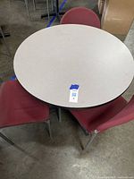 Top-down view of 36-inch round table with three surrounding red fabric upholstered chairs on concrete floor.