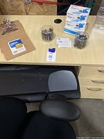 Partial close-up of desk surface showing clipboards, push pins in plastic containers, and small boxed blue office items.