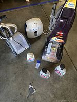 View of all items included: carpet cleaner, steamer, humidifier, and cleaning solutions on concrete floor.