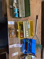 Three fishing tackle boxes and a fishing net on a wooden surface, showing various accessories inside boxes.