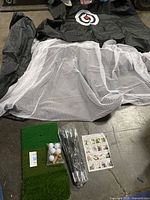 All items spread out: black net with target, white mesh netting, green turf mat, golf balls, tees, rods, and instructions.