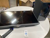 LG 32 inch LED TV flat screen alongside a black Samsung subwoofer on a table. Remote control visible in front of TV.