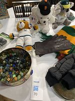 Lot items on round white table including MLB team plush toys, leather gloves, mittens, scarves and tin of marbles.