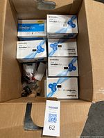 Full view of the open box showing 16 boxes of OfficeMax large binder clips in black, some with 12 clips 1-inch capacity and others 12 clips 2-inch capacity, along with some loose clips.