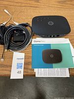 Ooma Telo VoIP device, power adapter with cable, Ethernet cable, and quick start guide laid out on wooden surface.