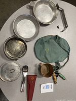 Top-down photo showing all cookware pieces, utensils, knife sheath, and green carrying bag spread on a surface.
