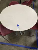 Top view of the 42-inch round white tabletop with 3 red chairs around it on a concrete floor.
